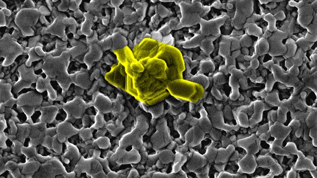 Scanning electron microscope (SEM) image showing the formation of methylammonium lead iodide perovskite (CH3NH3PbI3) by the reaction of lead iodide (PbI2) films with methylammonium iodide (CH3NH3I) solution for 2 seconds in the dark. The growth of a PbI2 crystal (highlighted in yellow) from the partly amorphous PbI2 film is visible. Image shows an area of 2.77 microns x 2.08 microns. @ EPFL